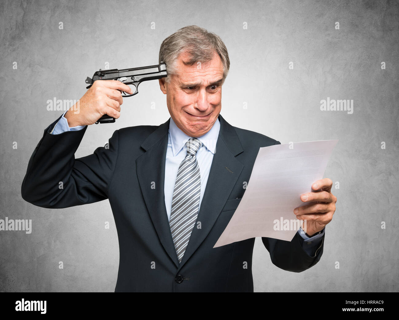 Desperate businessman pointing a gun to his head while reading a document Stock Photo