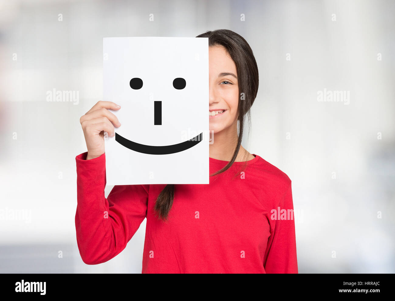 Happy girl covering her face with a smiley emoticon on a paper sheet Stock Photo