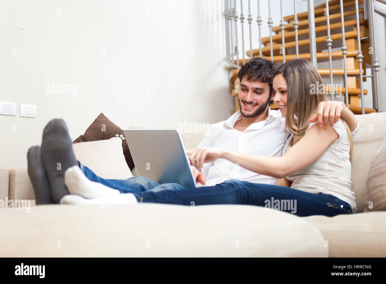 Young happy couple surfing on internet with their laptop in a modern apartment Stock Photo