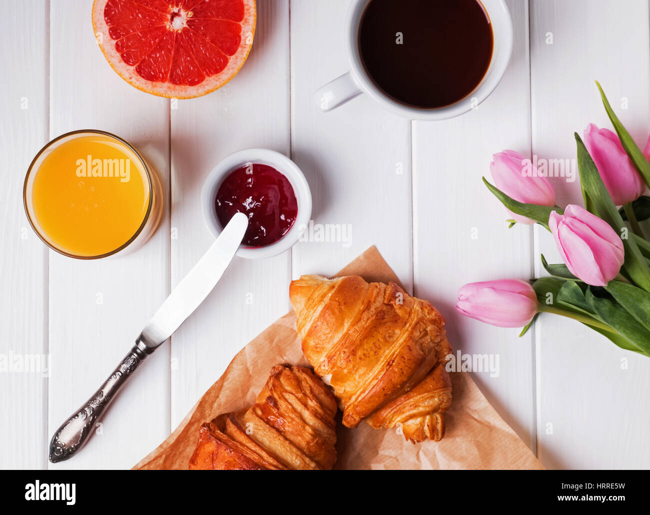 Delicious breakfast with croissants and coffee and pink tulips on the white wooden table, top view Stock Photo