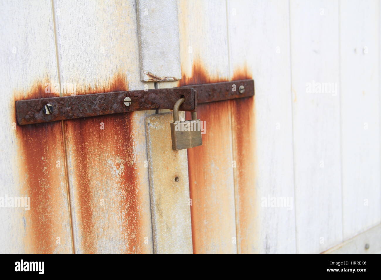 Old lock and rusty iron hasp on a white wooden door, with rust stains