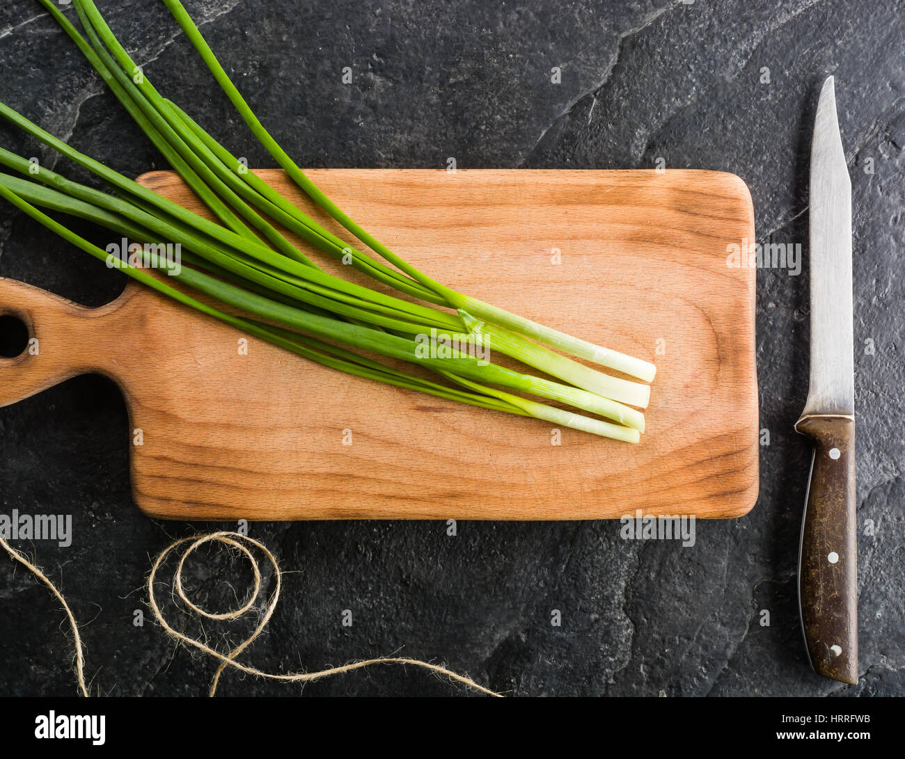 A bunch of green onions on a cutting board. Background black slate ...
