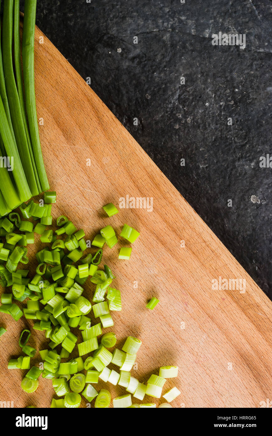 A bunch of green onions on a cutting board. Background black slate ...