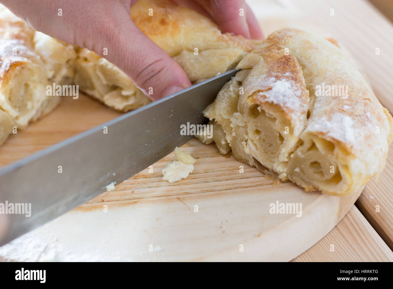 Female hands cut freshly baked cheese pie on the wooden plate Stock Photo