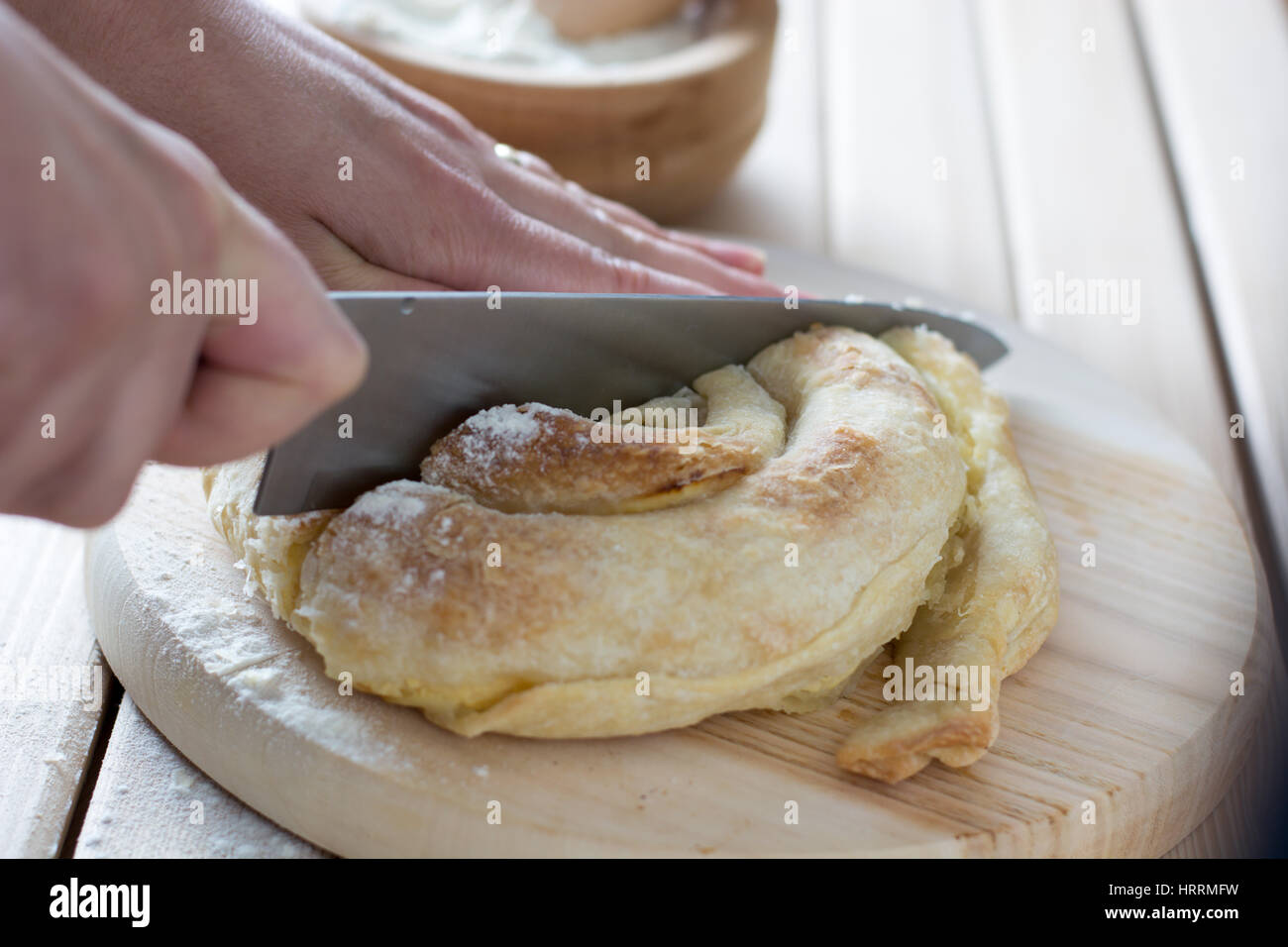Female hands cutting freshly baked cheese pie on the wooden plate Stock Photo