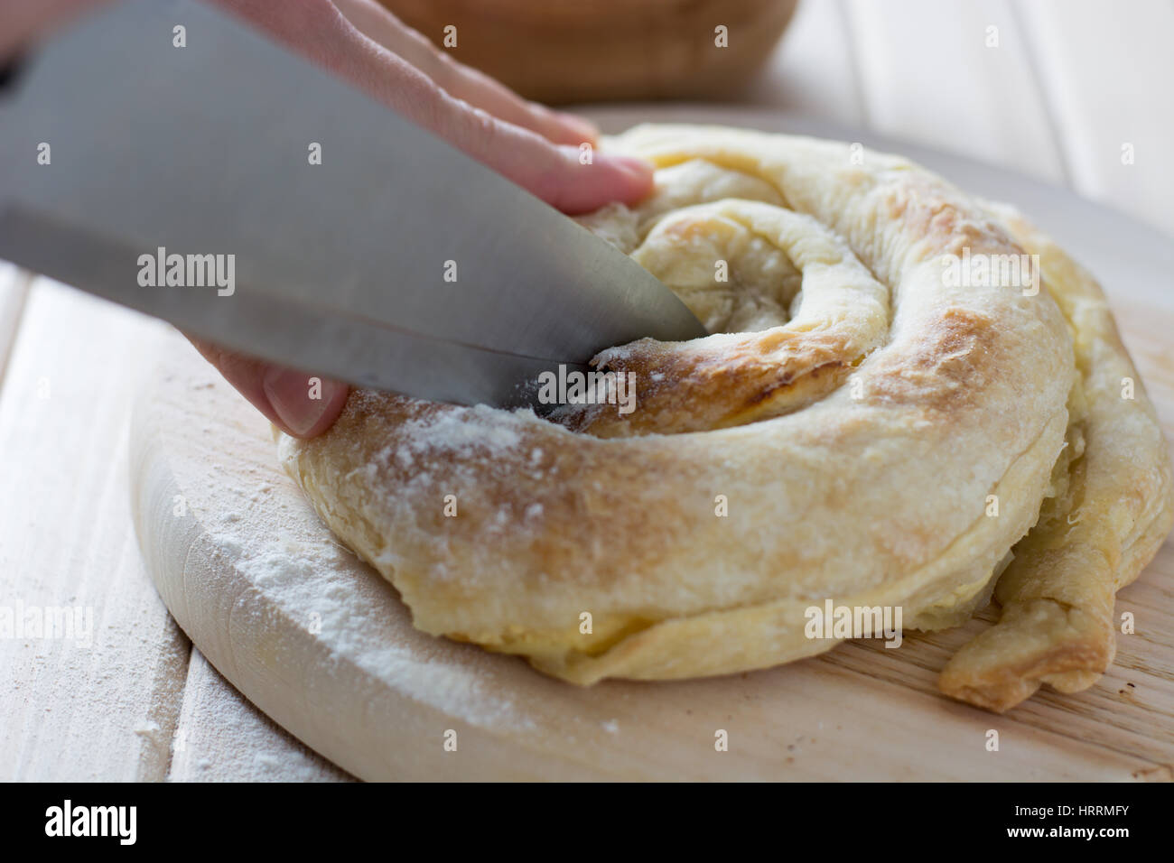 Female hands cutting freshly baked cheese pie on the wooden plate Stock Photo