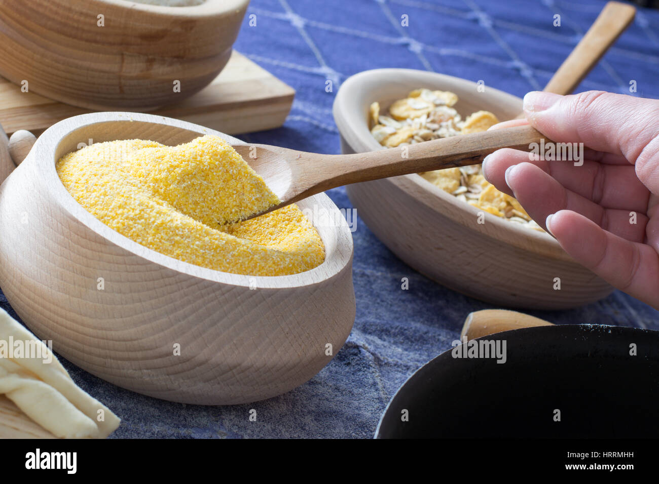 Female hand picking up corn flour with wooden spoon from wooden bowl on the home table Stock Photo