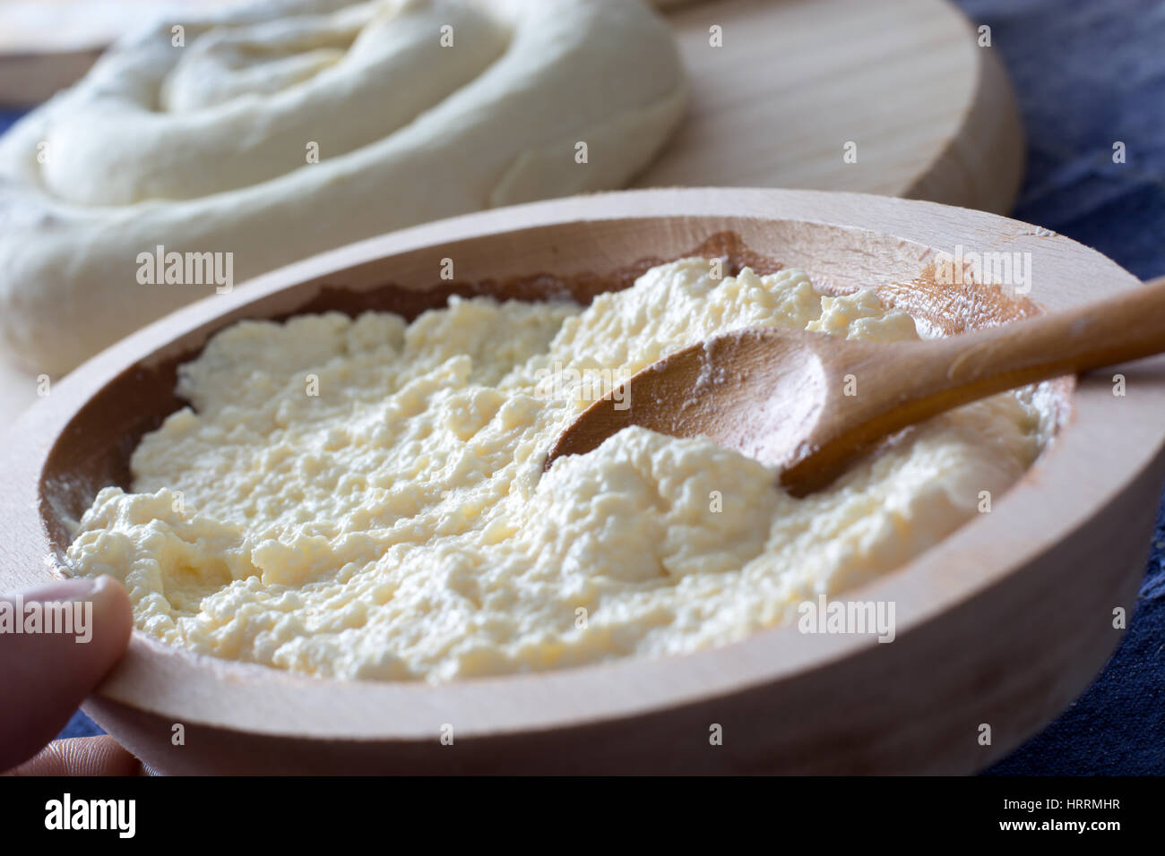 Molten cheese prepared for the cheese pie in the wooden bowl with spoon and female hand holding it. On the backround visible rolled cheese pie ready f Stock Photo
