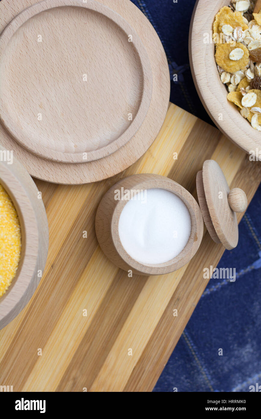 Salt in a small wooden bowl placed on the wooden plate with cereals and corn flour Stock Photo
