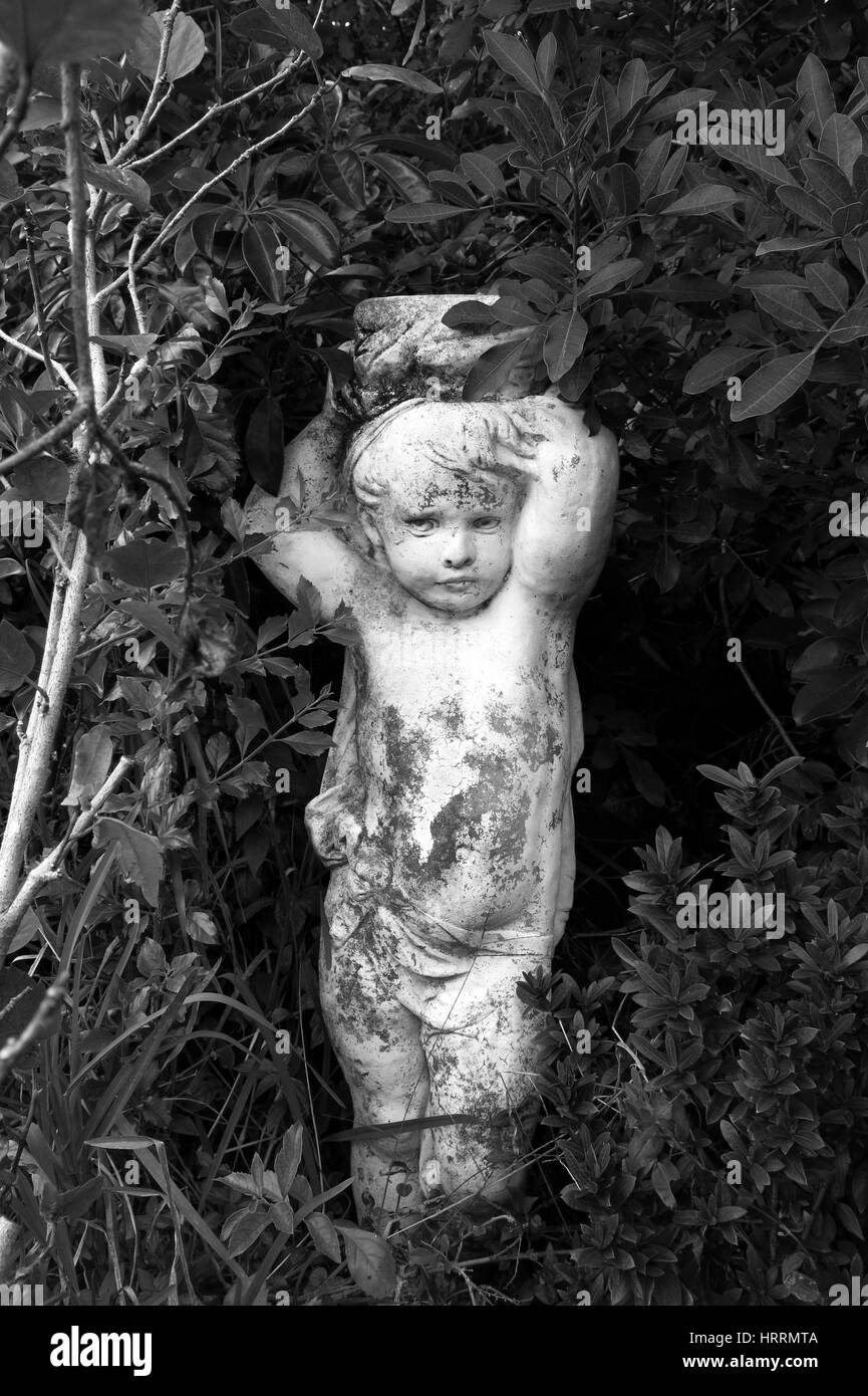 Black and white cherub child statue in tropical garden Stock Photo