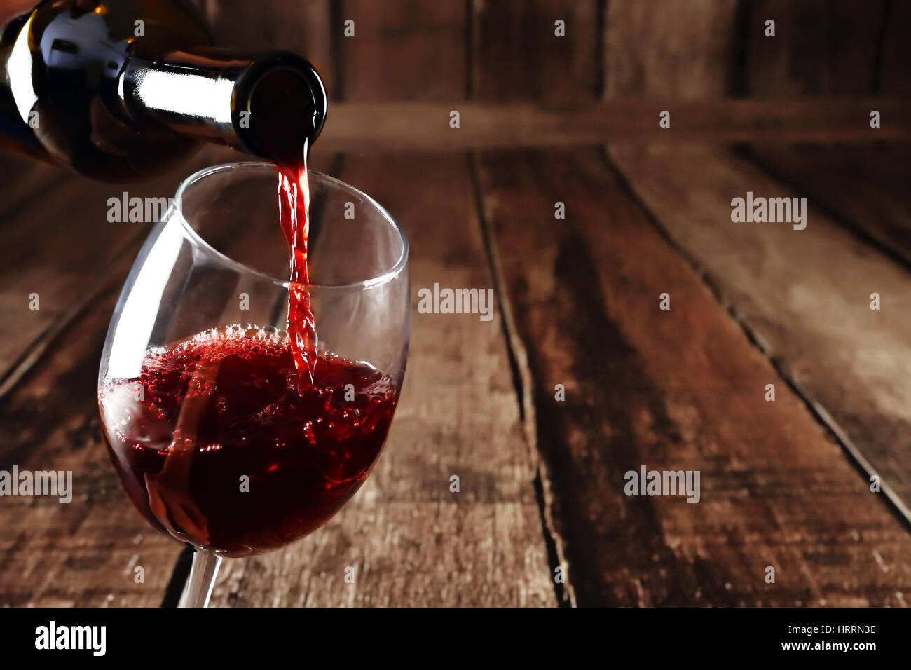 Red wine in glass on wooden background. Beautiful alcohol background. Red wine pouring from bottle. Free space for text on wooden backdrop. Stock Photo