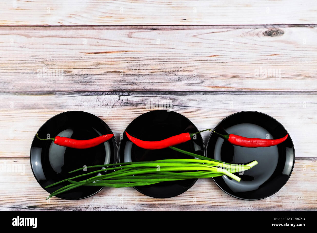 Red peppers on black dish. Green onions on black shiny plates. Vegetables in plates over wooden background. Colorful food background. Free space for t Stock Photo