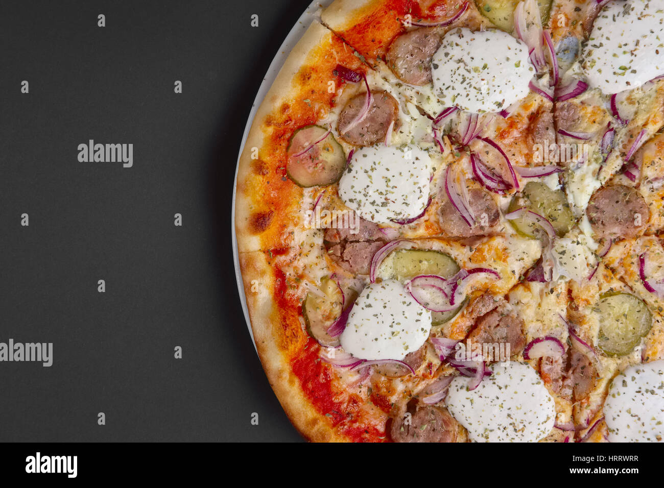 Top view of pizza with sausage, pickled cucumber, onion and horseradish