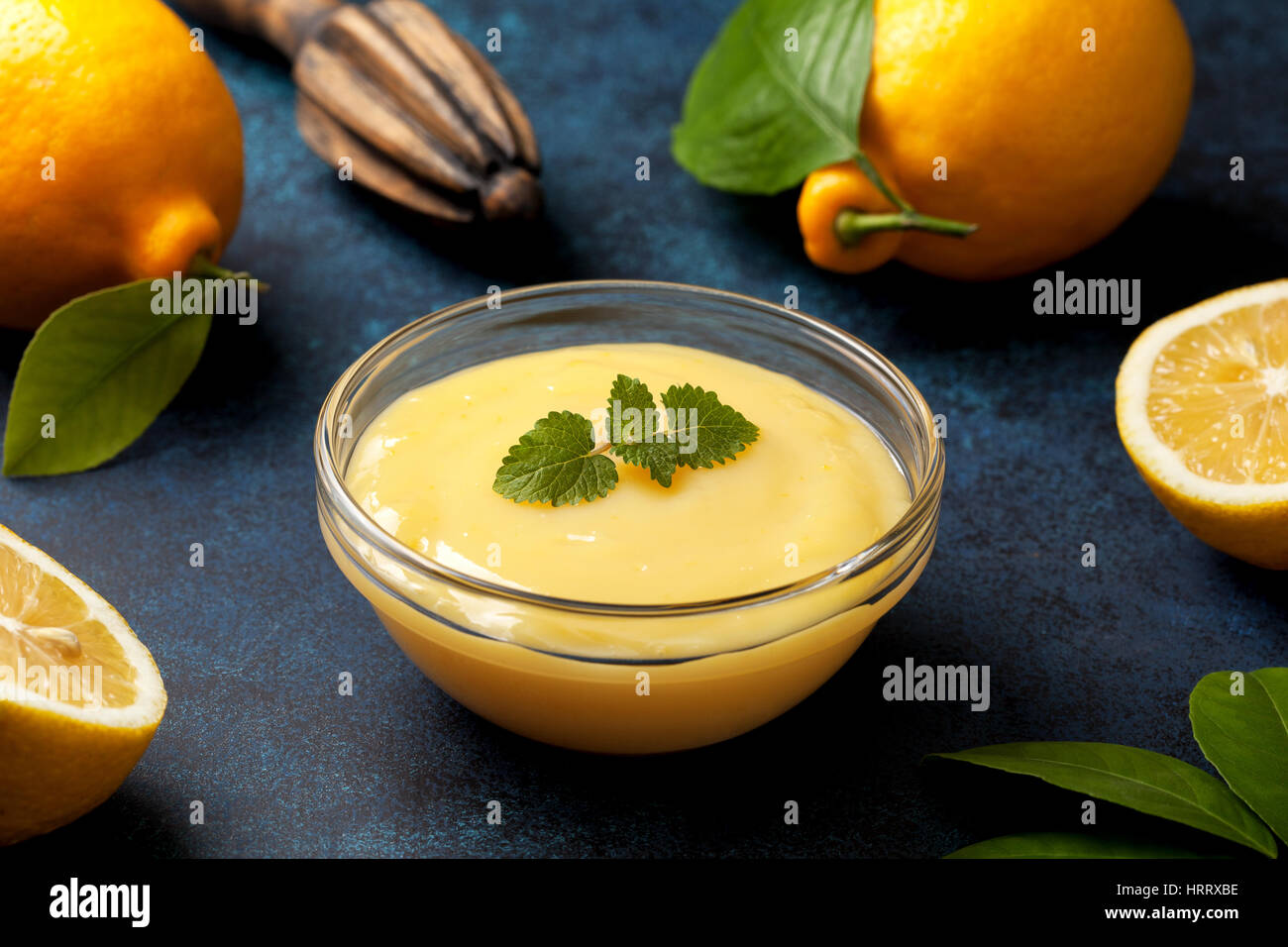 lemon curd in a glass bowl, fresh lemons, juicer on a blue background