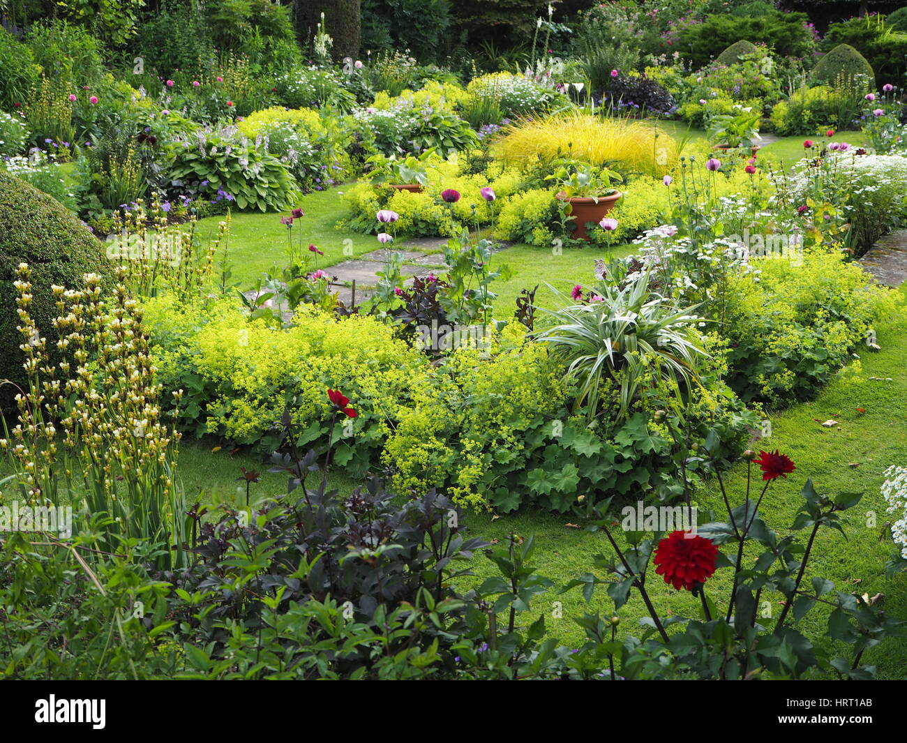 Chenies Manor Sunken garden in summertime with dahlias and lush green foliage plants around the ornamental pond and herbaceous borders; grassy paths. Stock Photo