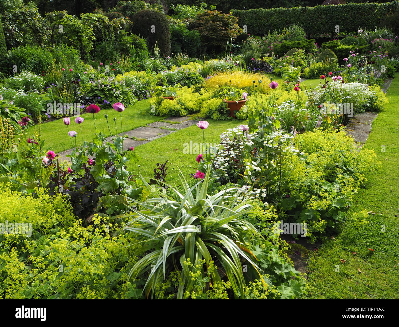 Chenies Manor Sunken garden in summertime with dahlias and lush green foliage plants around the ornamental pond and herbaceous borders; grassy paths. Stock Photo