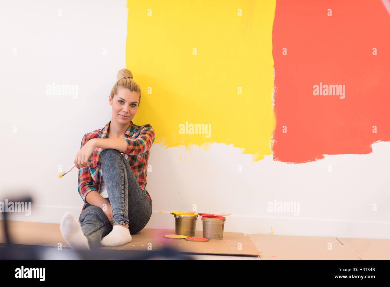 Portrait of a beautiful young female painter sitting on floor near wall ...