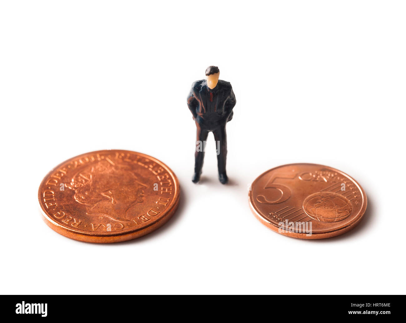 Miniature figure of male businessman standing on white background between UK sterling and Euro coin Stock Photo