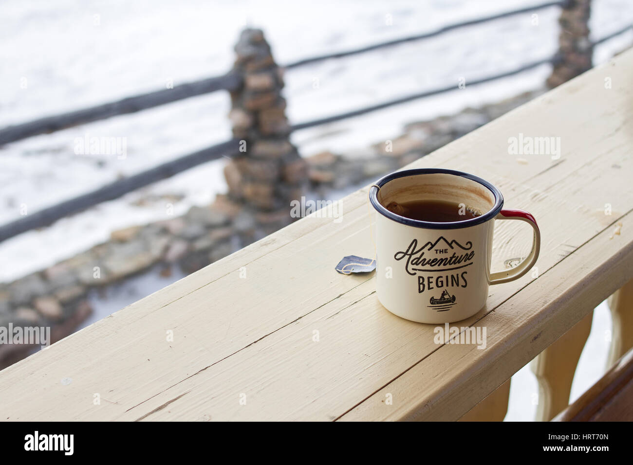 Enamel mug with strong tea and tea bag on a wooden fence on a snowy winter background. Stock Photo
