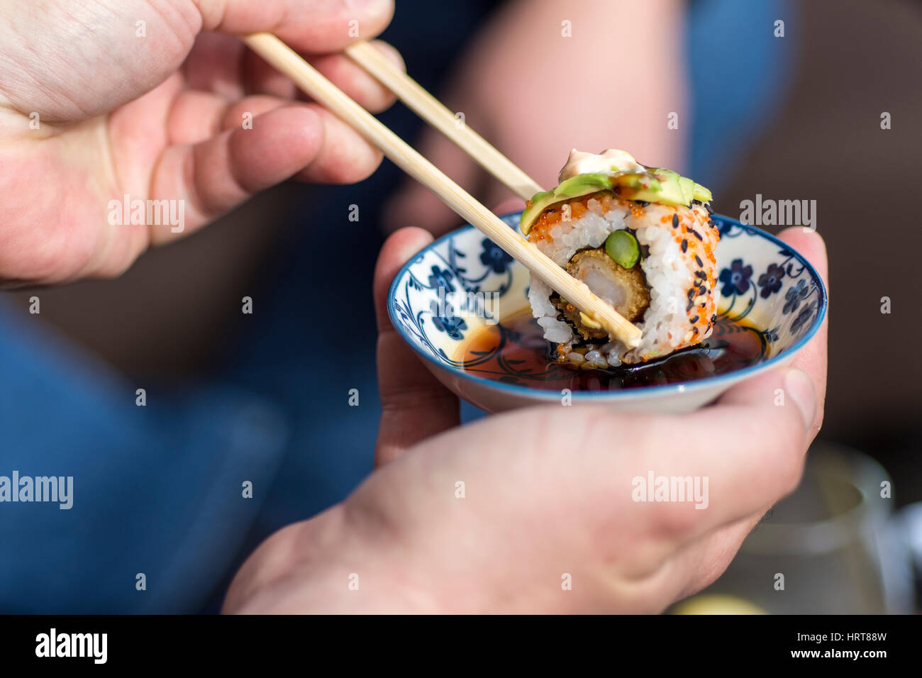 Male Hand Holding Chopsticks to Dip Sushi Roll in the Soy Sauce Stock