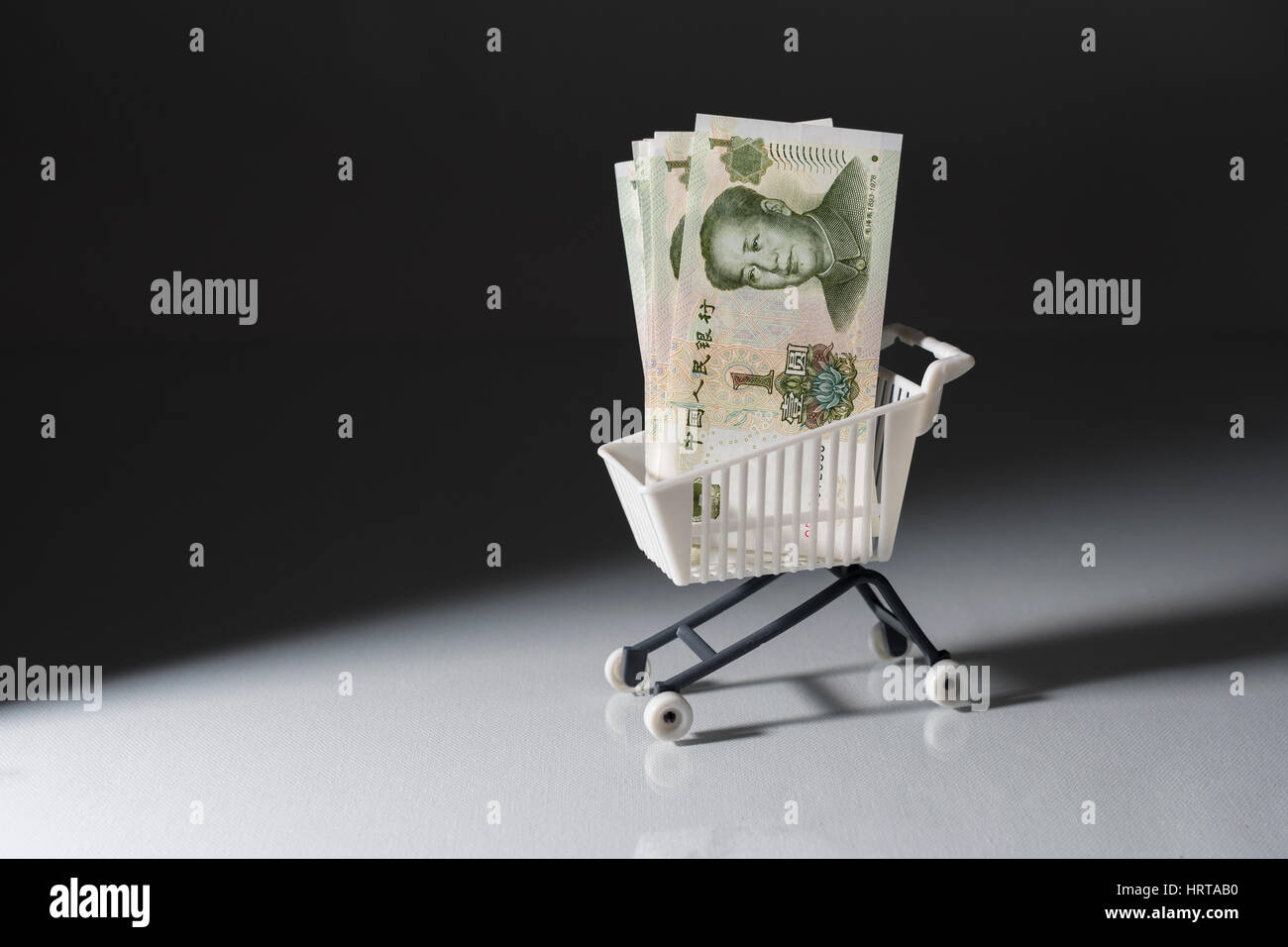 1 Yuan bills / banknotes in shopping cart / trolley against dark background. Metaphor for Chinese economy, budget, spending power, consumer spending. Stock Photo