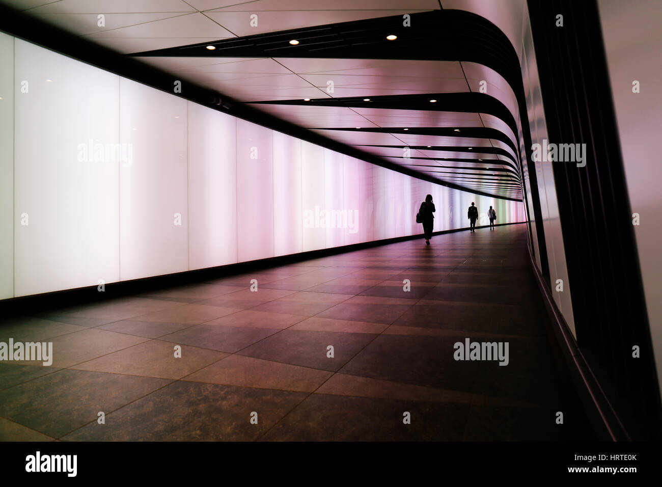 People walking through futuristic looking pedestrian tunnel featuring an LED integrated light wall in Granary Square exit from Kings Cross Underground Stock Photo