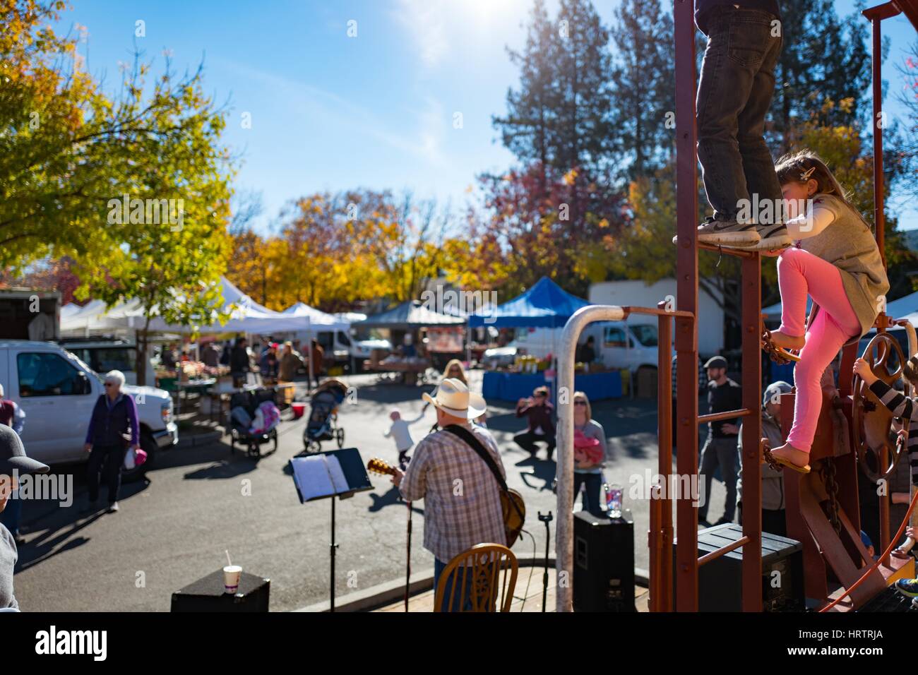 Children climb and play on a ladder while a bluegrass musician plays music during a farmer's market in Danville, California, December 3, 2016. Stock Photo