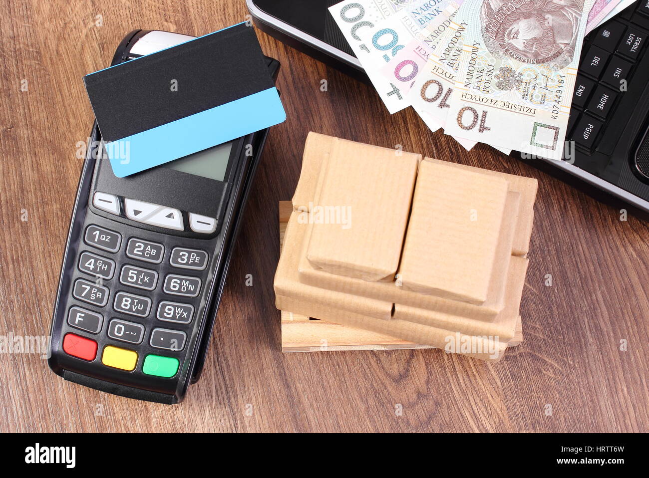 Payment terminal with contactless credit card, polish currency money, laptop and small wrapped boxes on wooden pallet, paying for products and shippin Stock Photo