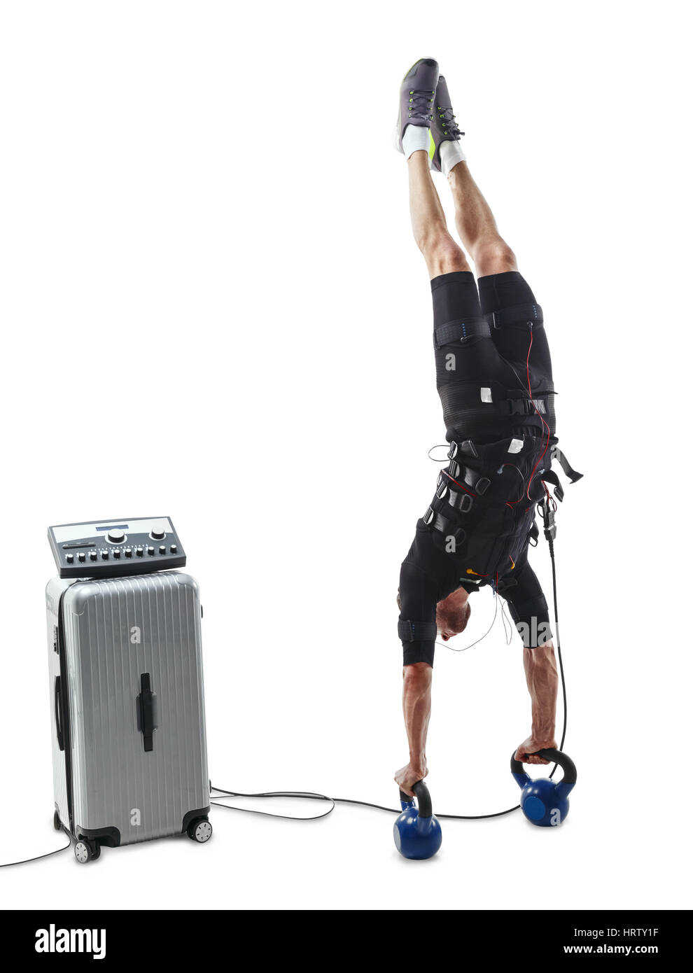 Fitness athlete in electrical muscular stimulation suit doing a vertical handstand upside down on dumbbells. Isolated on white background. Stock Photo