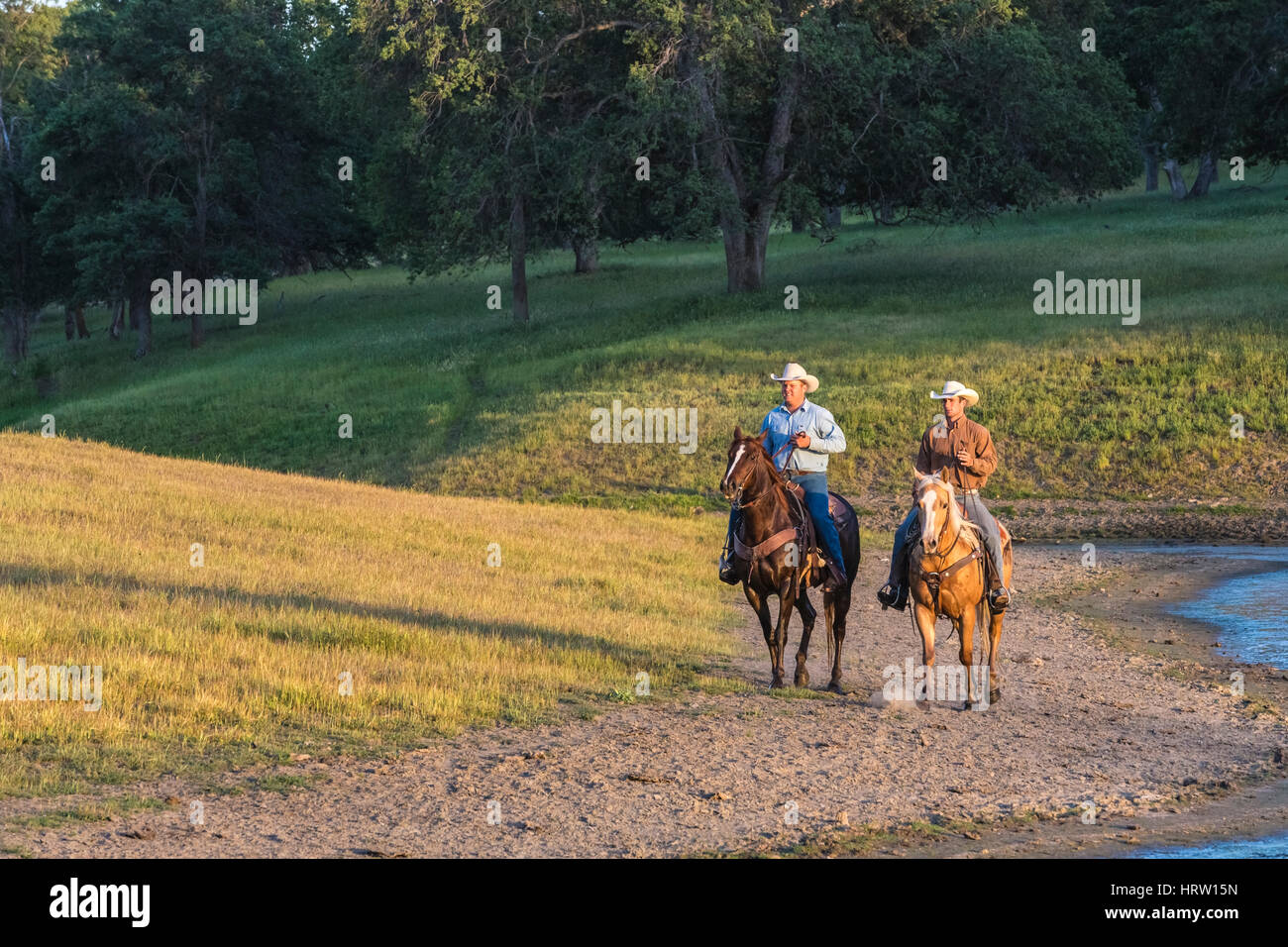 two cowboys on horseback crossing creek on ranch Stock Photo
