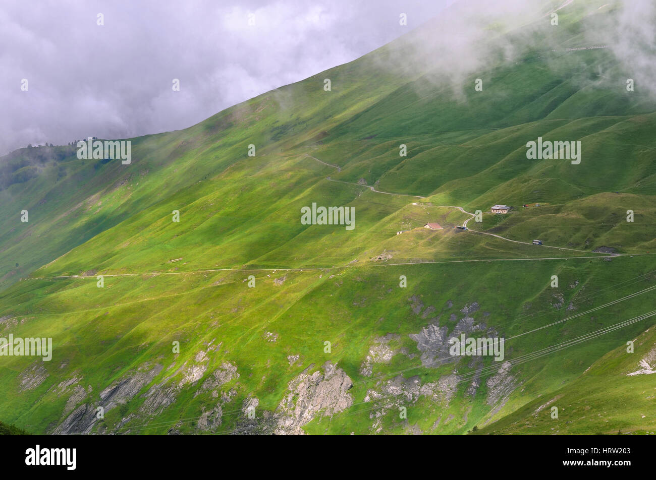 green meadow in mountain under cloudy sky Stock Photo