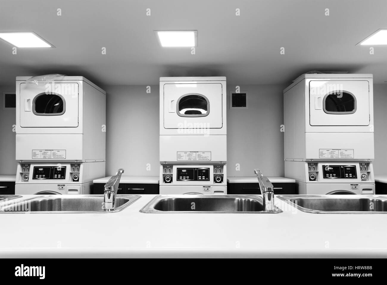 Line of big self-service washing machines and dryers and laundry next to water sinks and taps in tabletop waiting for customers Stock Photo
