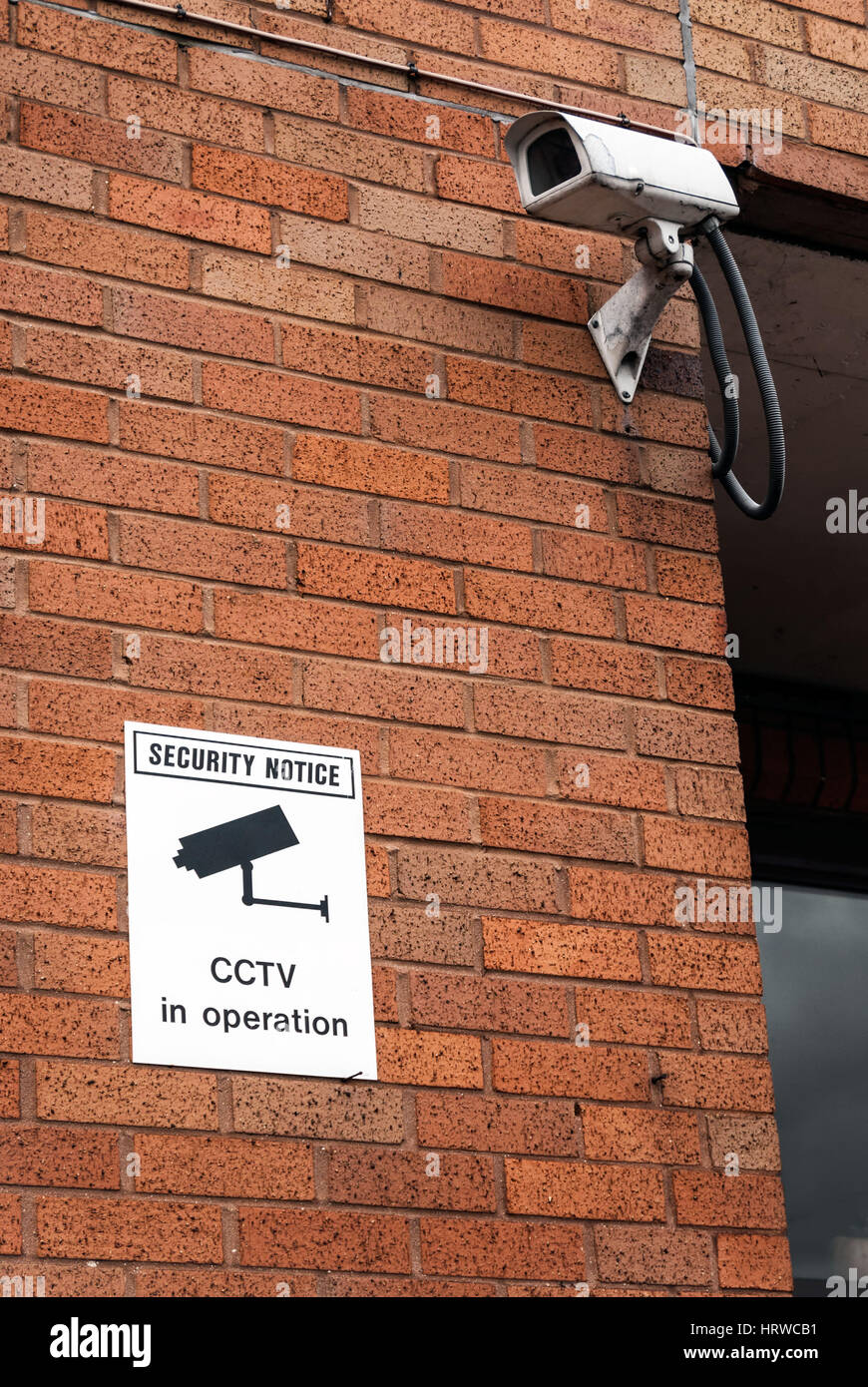 CCTV camera and warning notice on urban red brick wall Stock Photo