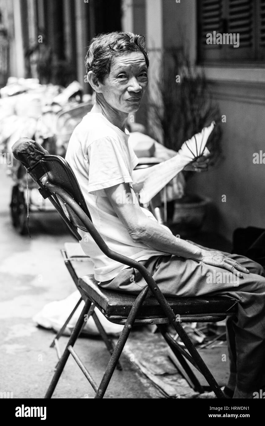 Hanoi, Vietnam - April 25, 2014: Vietnamese senior man restnig on his chair with fan on the street of Hanoi, Vietnam on April 25, 2014. Stock Photo