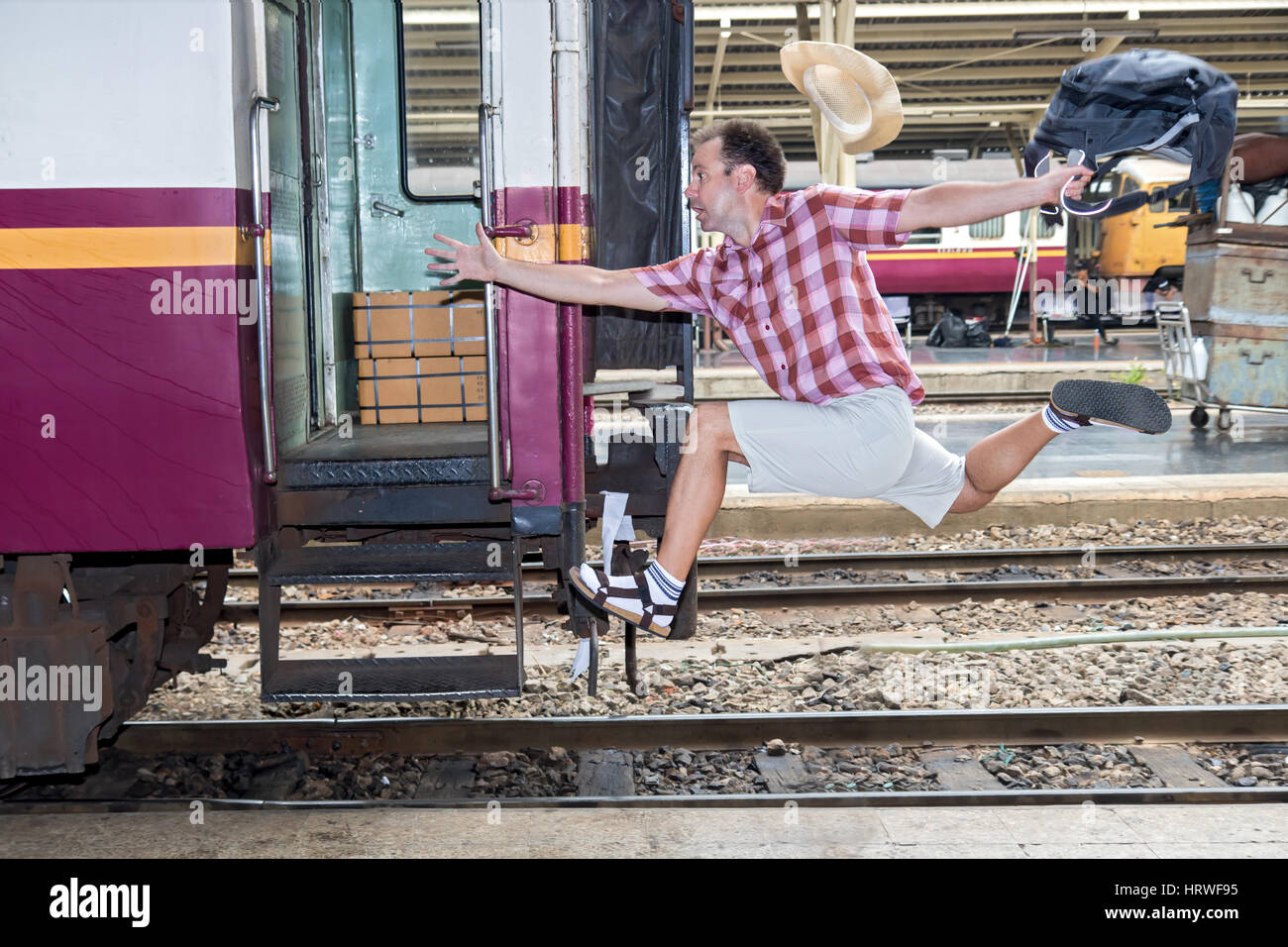Tourist with bag running behind the train. A man runs for a wagon. Backpacker hurries for train departing from the station. Journey to the last minute Stock Photo