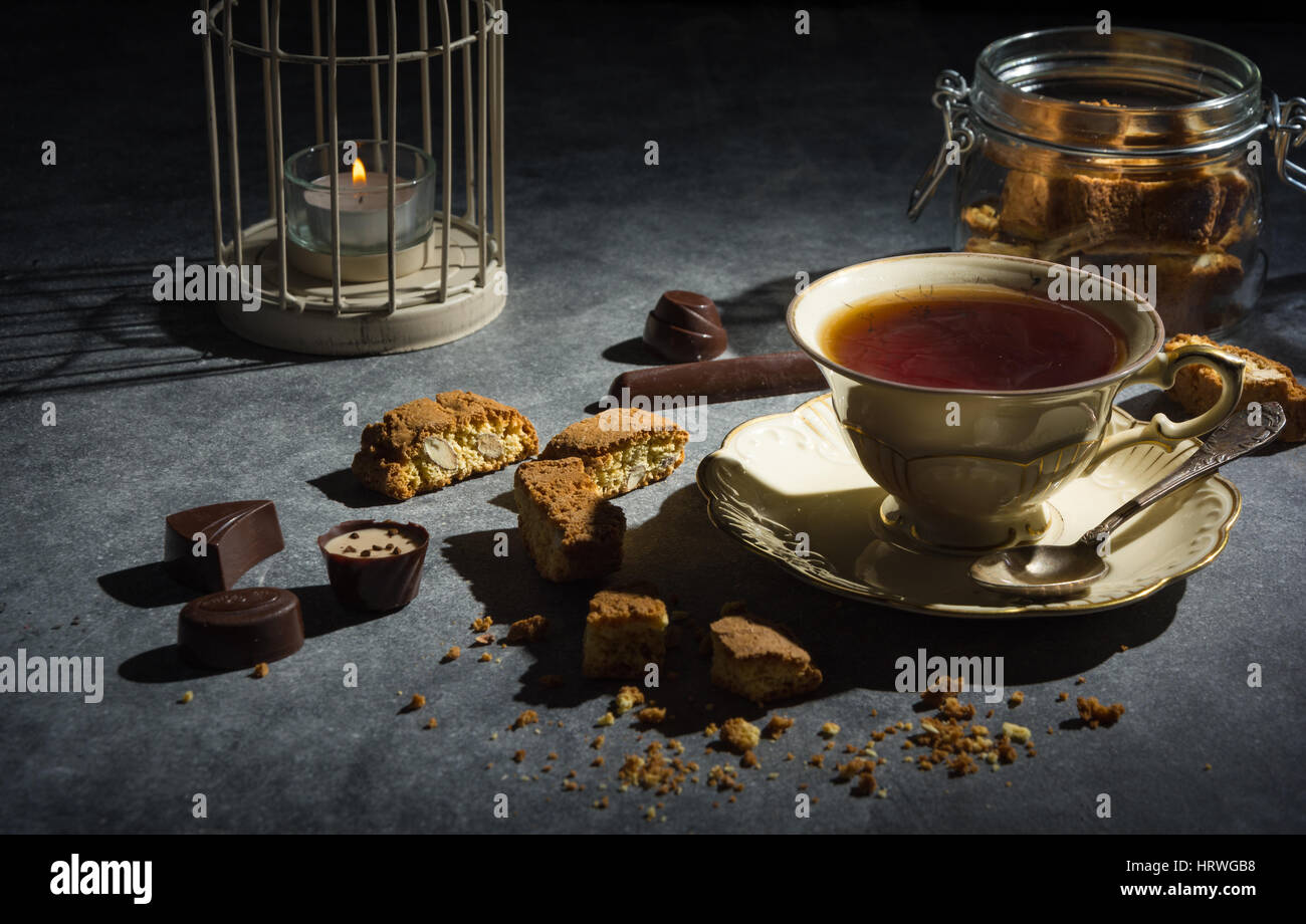 Cup of tea , tasty and healthy almond cookies, rich in vitamins, minerals in a glass jar and chocolates on a dark background. Low key. Stock Photo