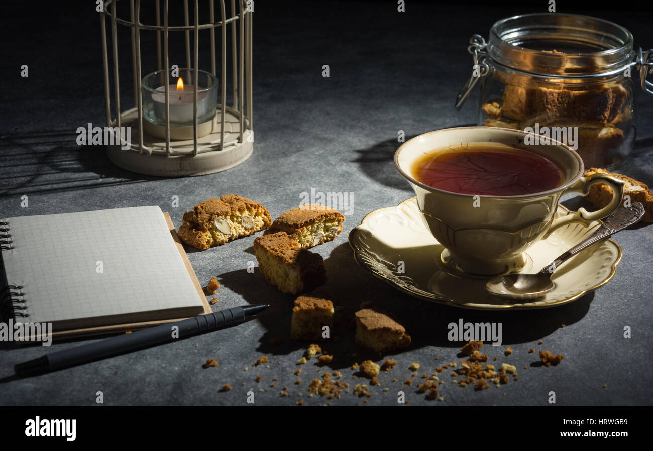 Cup of tea , tasty and healthy almond cookies, rich in vitamins, minerals in a glass jar and notebook on a dark background in low key. Copy space. Stock Photo