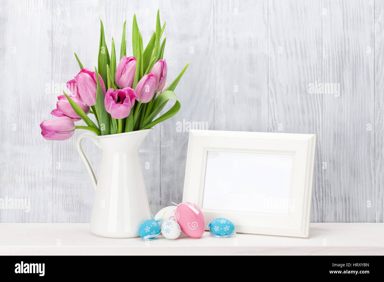 Easter eggs, blank photo frame and pink tulips bouquet on shelf in ...