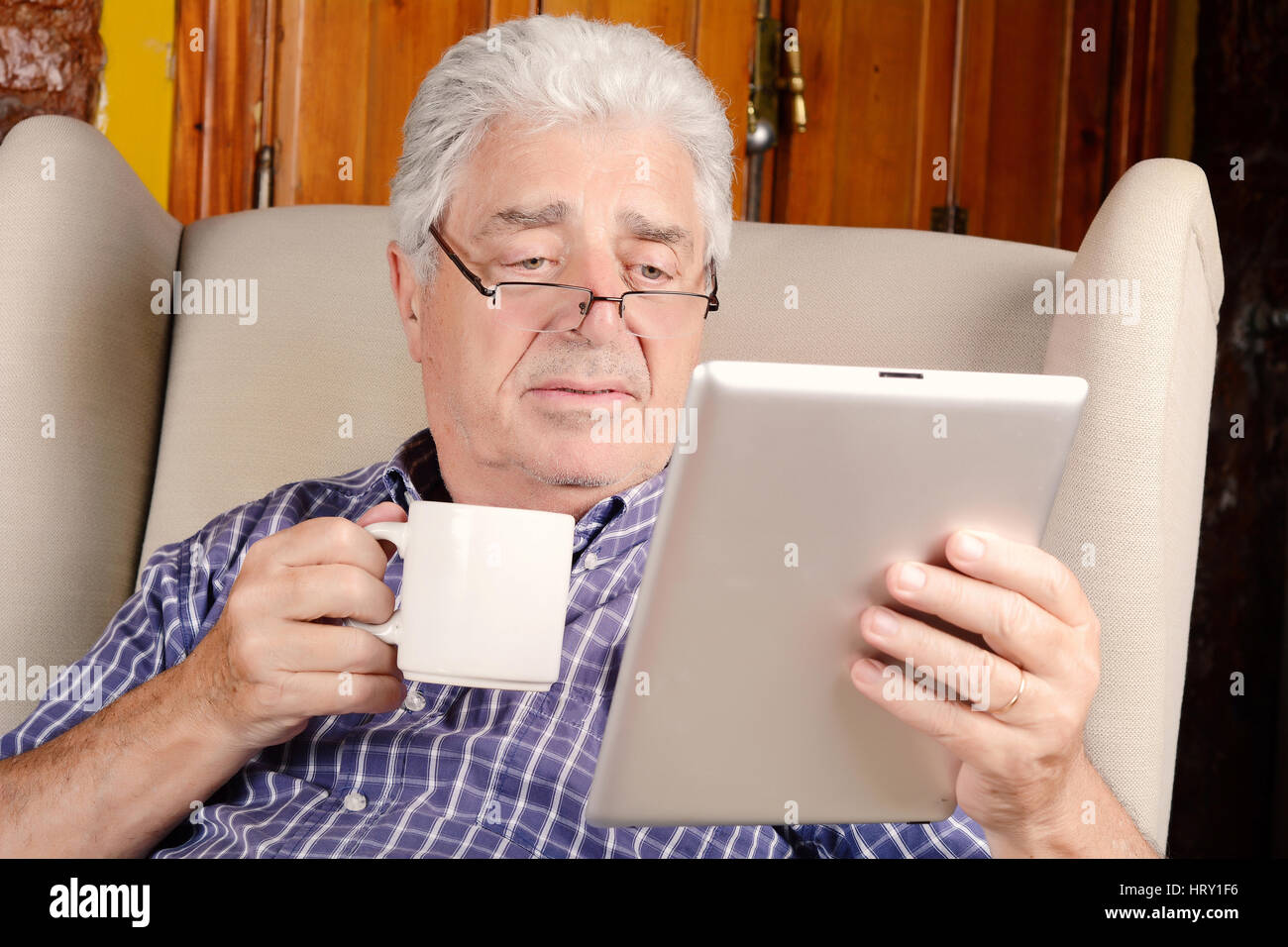 Portrait of an old man having a cup of coffee and using digital tablet. Indoors. Stock Photo