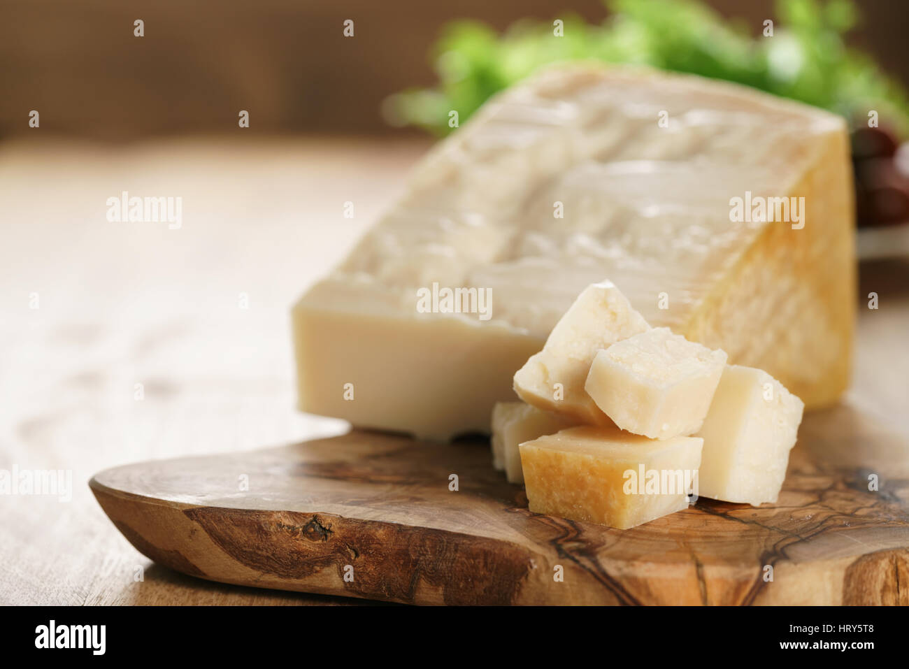 hard parmesan cheese cubes on olive cutting board, closeup photo Stock Photo