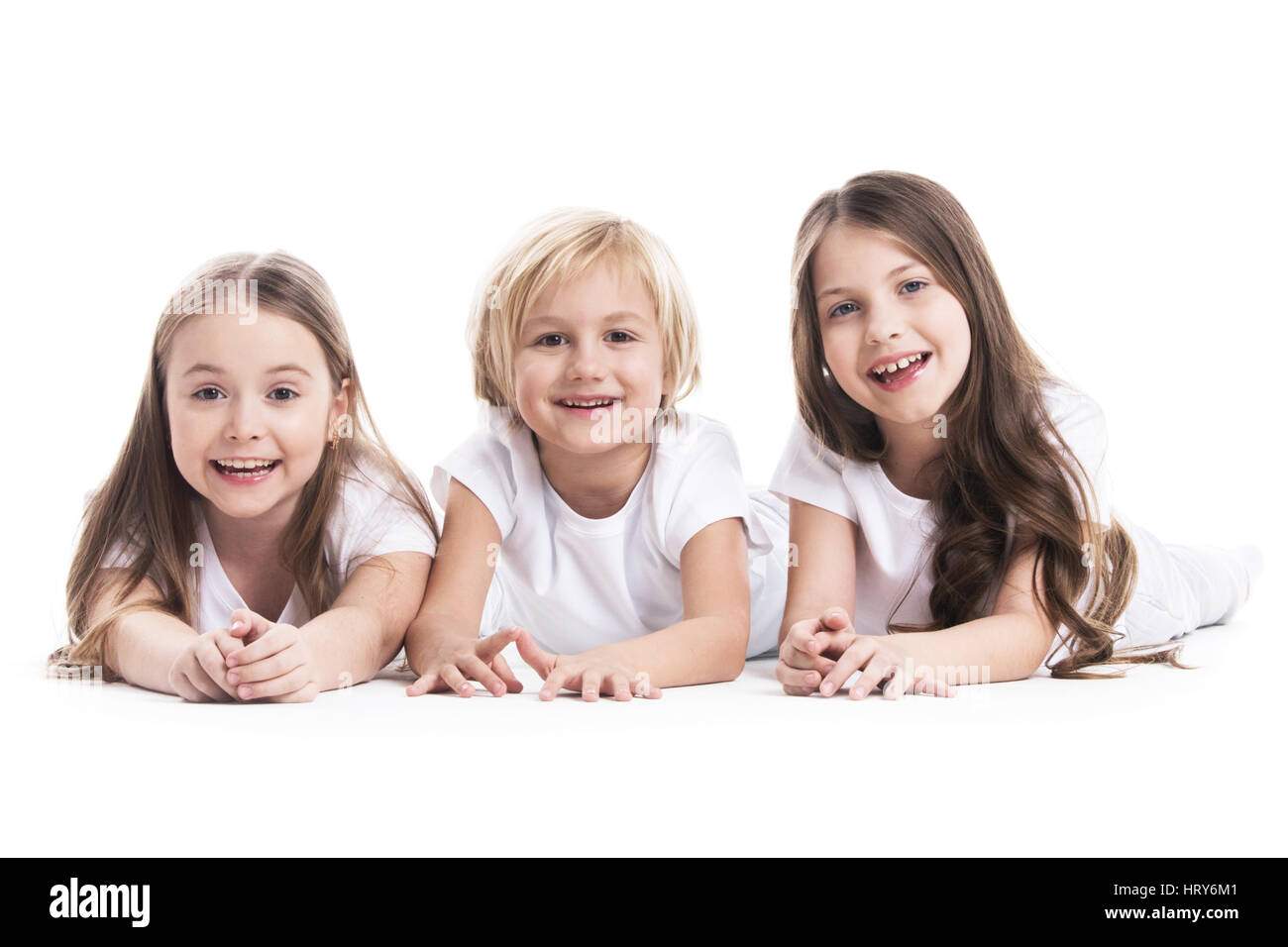 Happy smiling three children in white clothes laying on floor isolated on white background Stock Photo