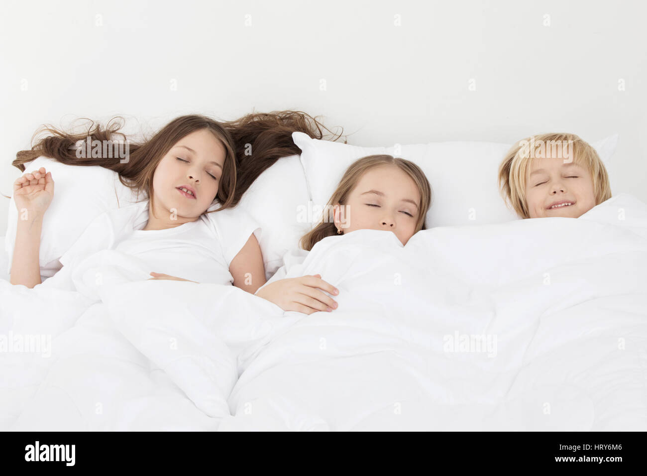 Three beautiful children sleeping in bed under one white blanket Stock
