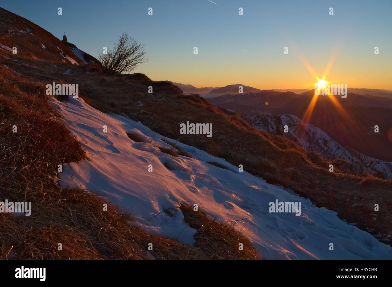 Sunrise on the Italian Alps during the winter with a bit of snow covering the dry grass Stock Photo