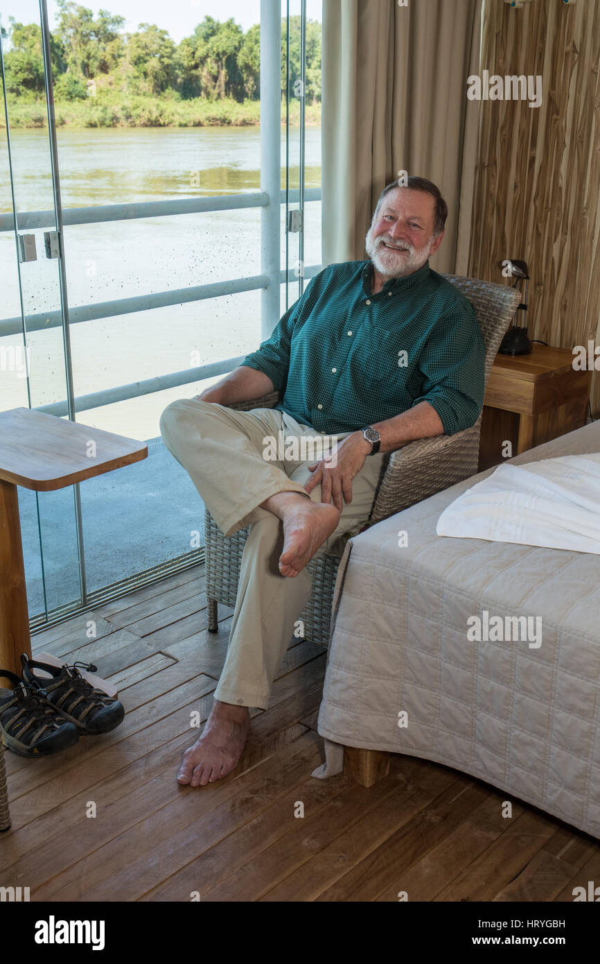 Man in his late sixties relaxing in his room in a floating hotel (flotel), after a morning on safari looking for jaguars, in the Pantanal region, Mato Stock Photo