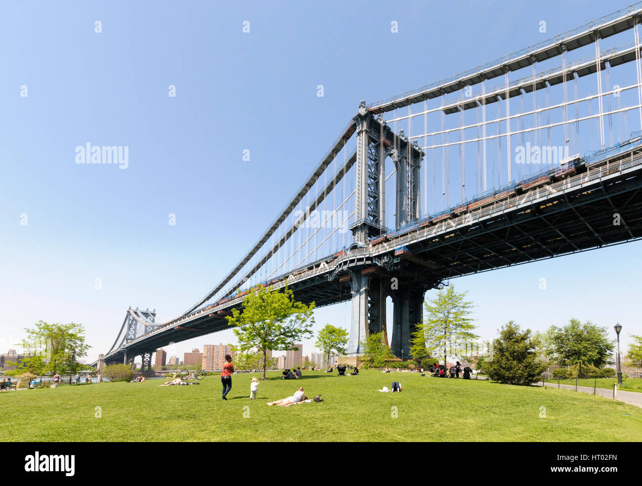 People relaxing in  Brooklyn bridge Park under the shadow of Brooklyn Bridge, New York City, USA Stock Photo