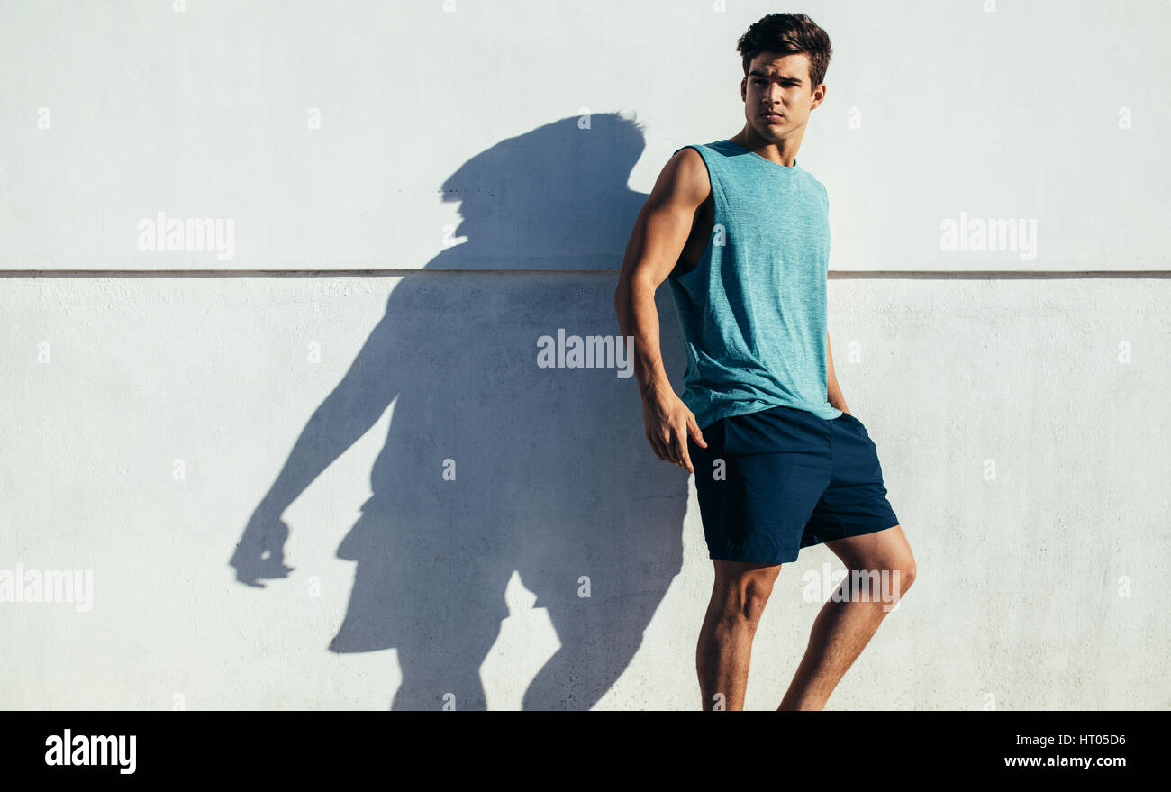 Shot of healthy young man standing against a wall outdoors. Fit young male relaxing after running exercise. Stock Photo
