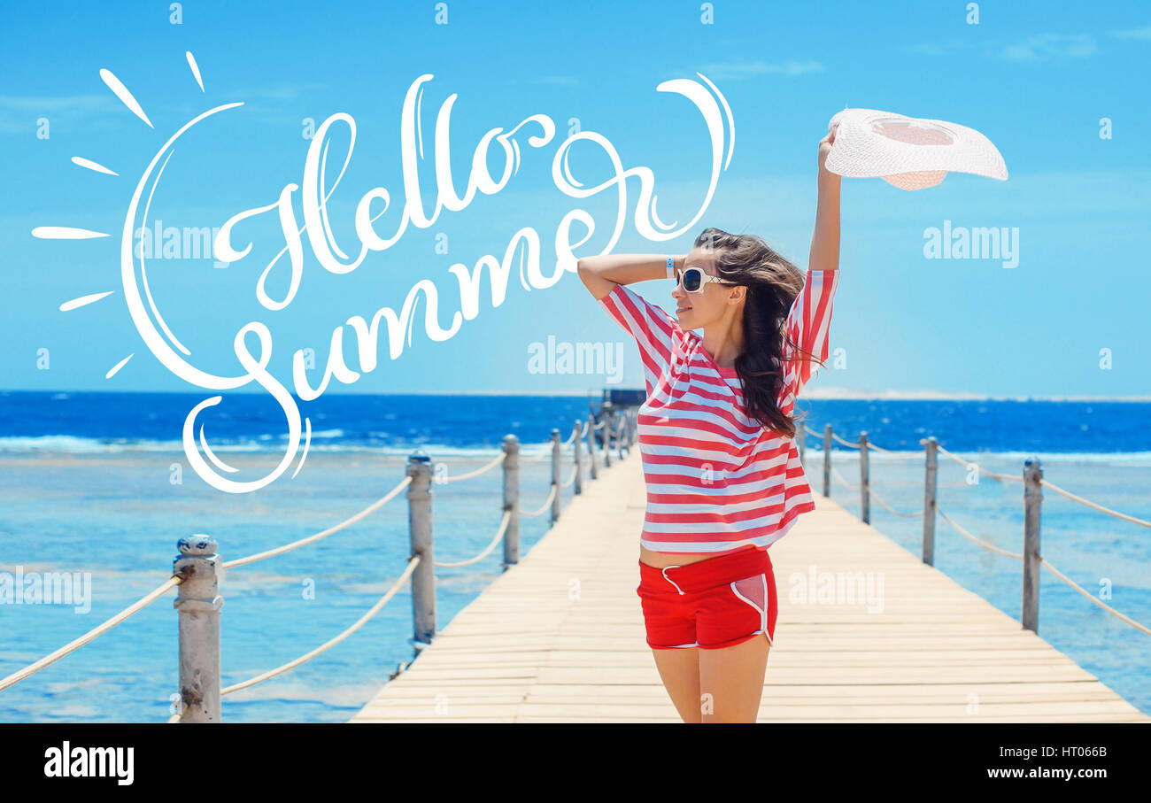 happy woman standing on pier with big white hat and text Hello Summer. Calligraphy lettering Stock Photo