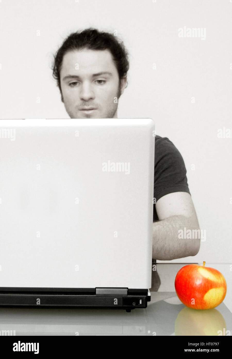 Mann arbeitet am Notebook, daneben liegt ein Apfel - man using laptop, aside an apple Stock Photo