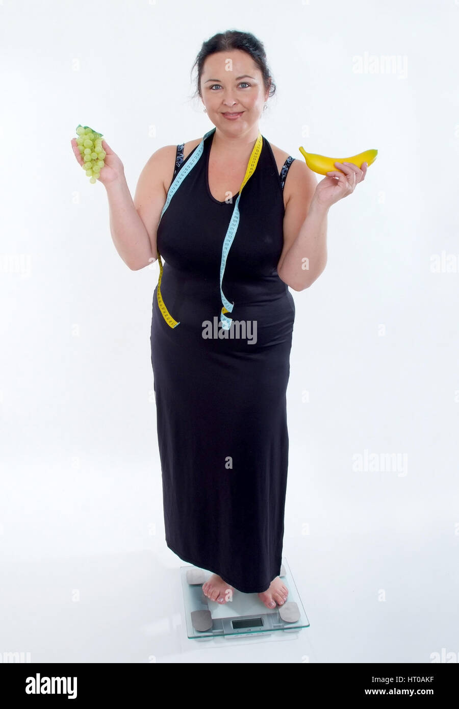 Selbstbewusste, mollige Frau steht mit Obst auf der Waage - chubby woman with fruits on scale Stock Photo