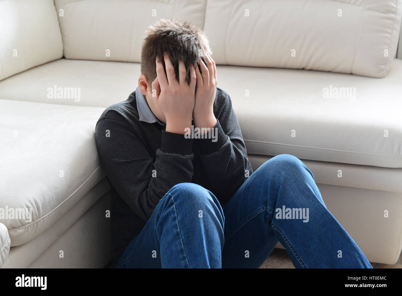 Upset teenager 13 years, he sits near sofa covering her face with her hands Stock Photo